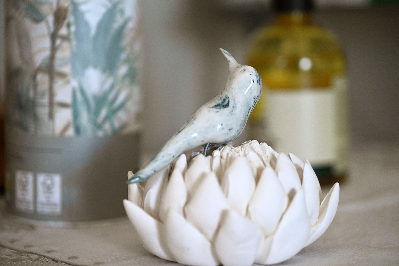 A small hand-painted ceramic bird figurine perched on a dried protea seed head.
